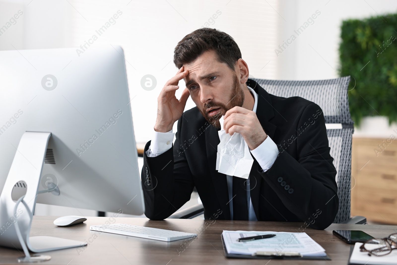 Photo of Sick man with runny nose at table in office