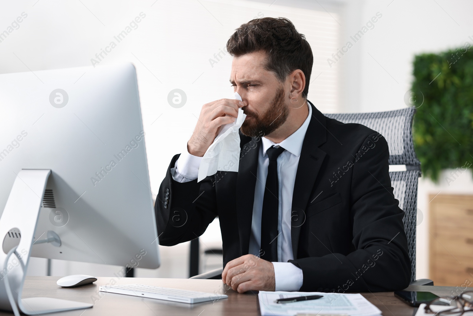 Photo of Sick man with runny nose at table in office