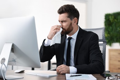 Photo of Sick man with runny nose at table in office