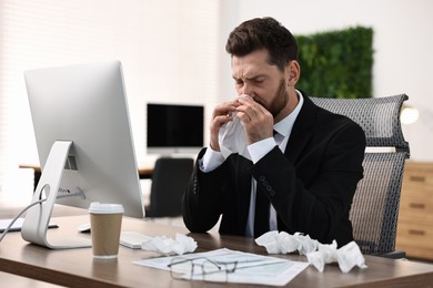 Photo of Sick man with runny nose at table in office