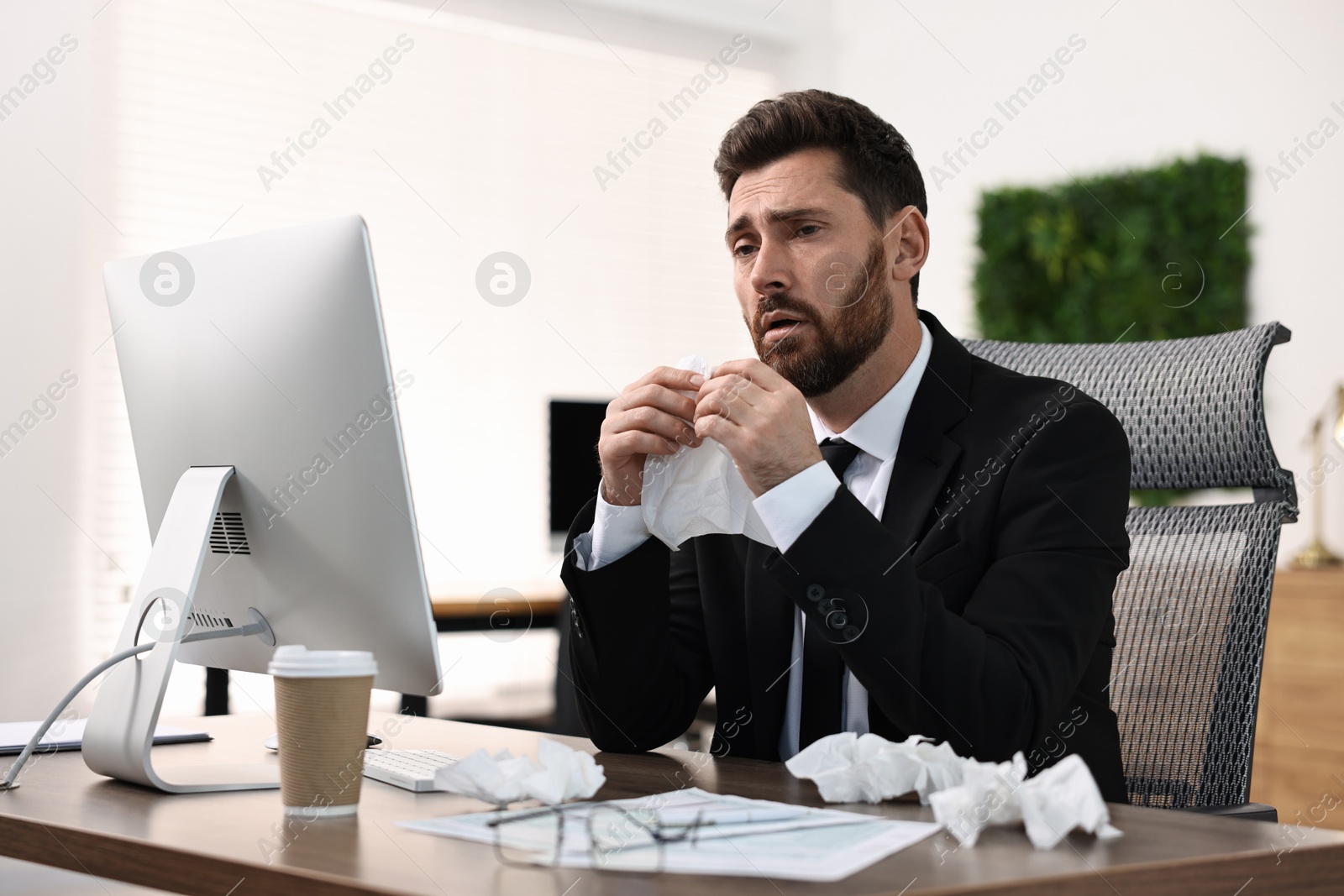 Photo of Sick man with runny nose at table in office