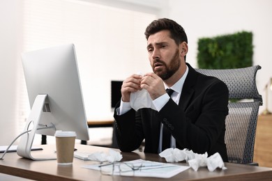 Photo of Sick man with runny nose at table in office