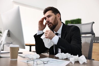 Photo of Sick man with runny nose at table in office