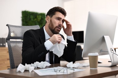 Photo of Sick man with runny nose at table in office