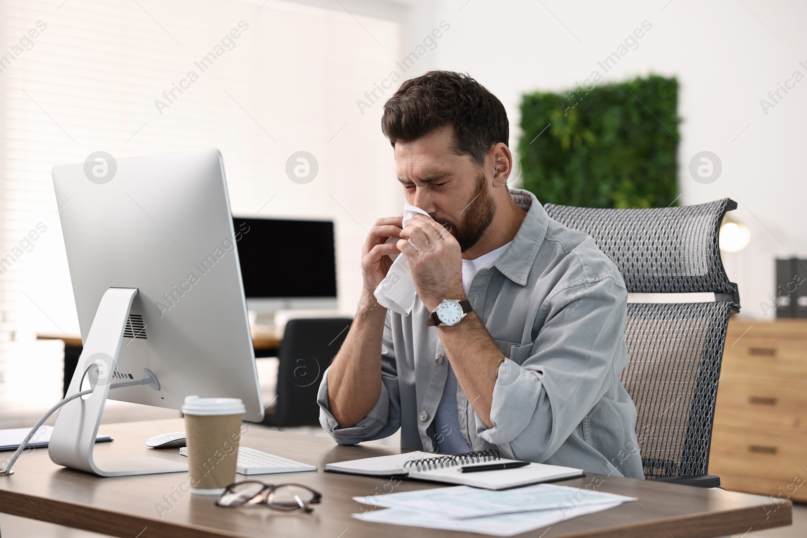 Photo of Sick man with runny nose at table in office