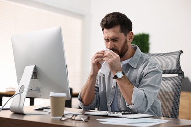 Photo of Sick man with runny nose at table in office