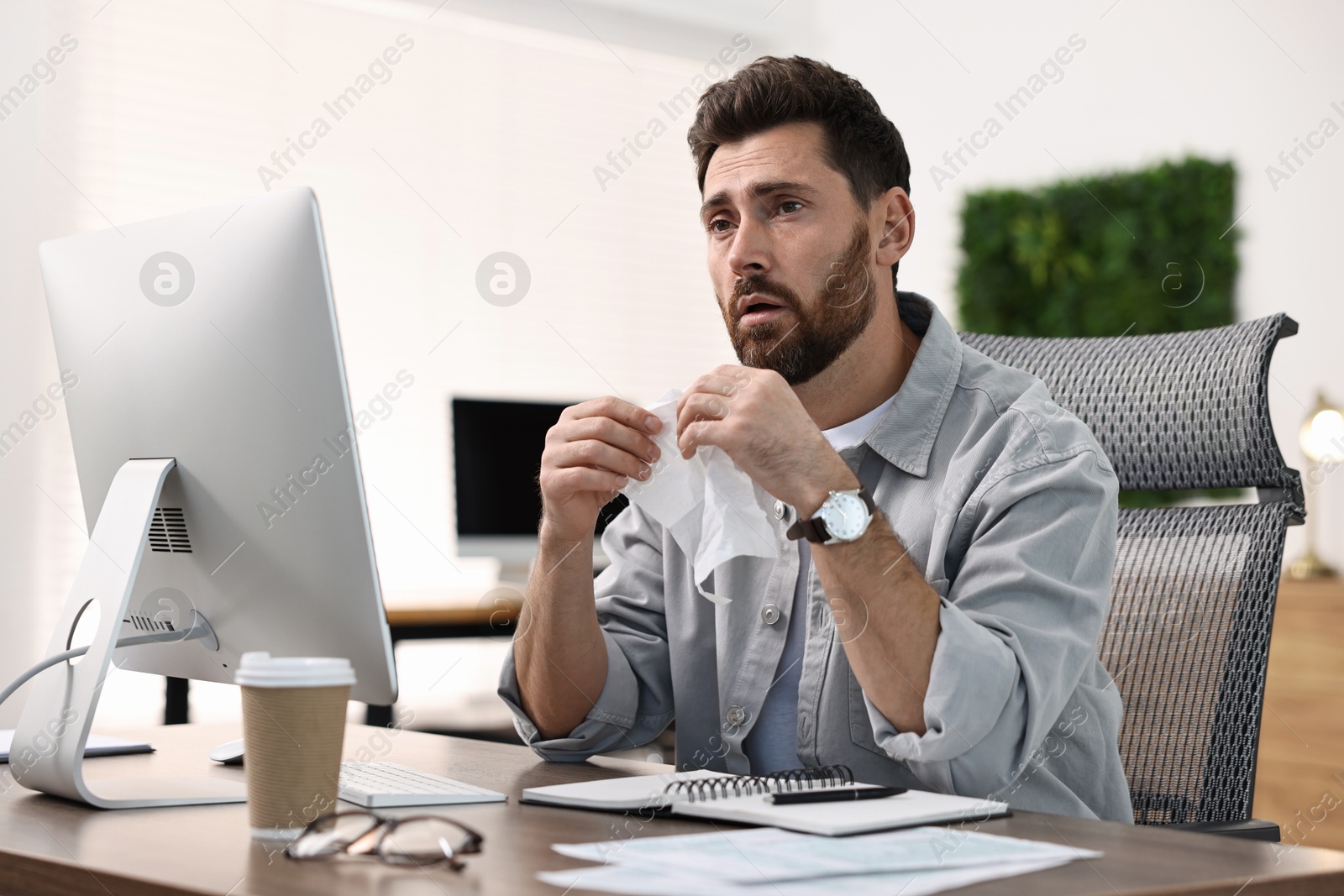 Photo of Sick man with runny nose at table in office