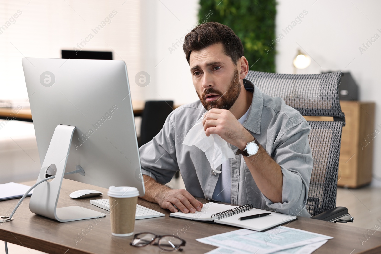 Photo of Sick man with runny nose at table in office