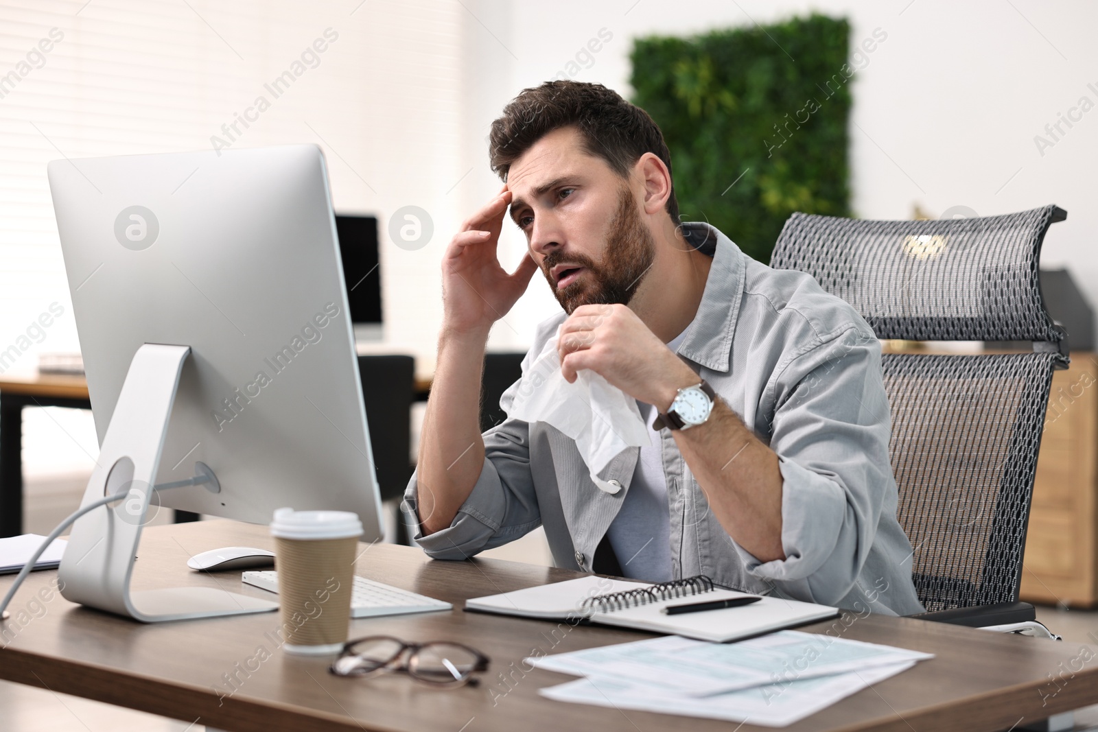 Photo of Sick man with runny nose at table in office