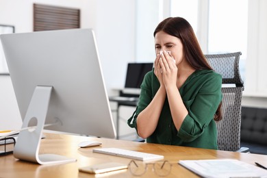 Photo of Sick woman with runny nose at table in office