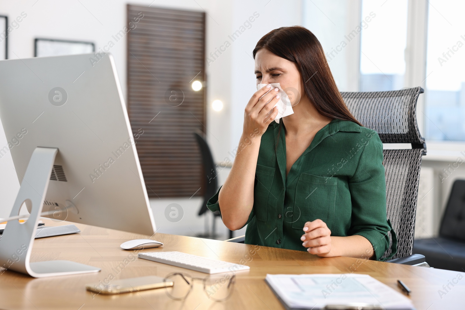 Photo of Sick woman with runny nose at table in office