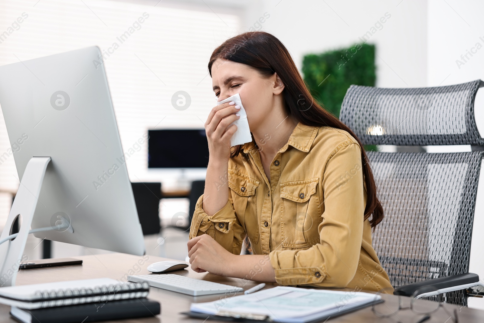 Photo of Sick woman with runny nose at table in office