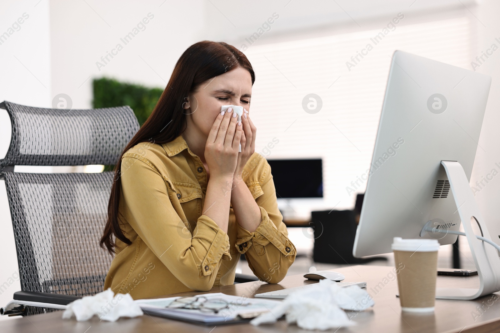 Photo of Sick woman with runny nose at table in office