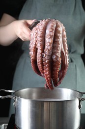 Photo of Woman taking boiled octopus from pan on stove, closeup