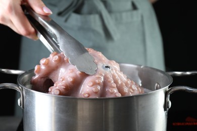 Photo of Woman taking boiled octopus from pan on stove, closeup