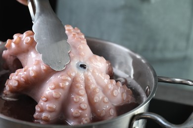 Photo of Woman taking boiled octopus from pan on stove, closeup