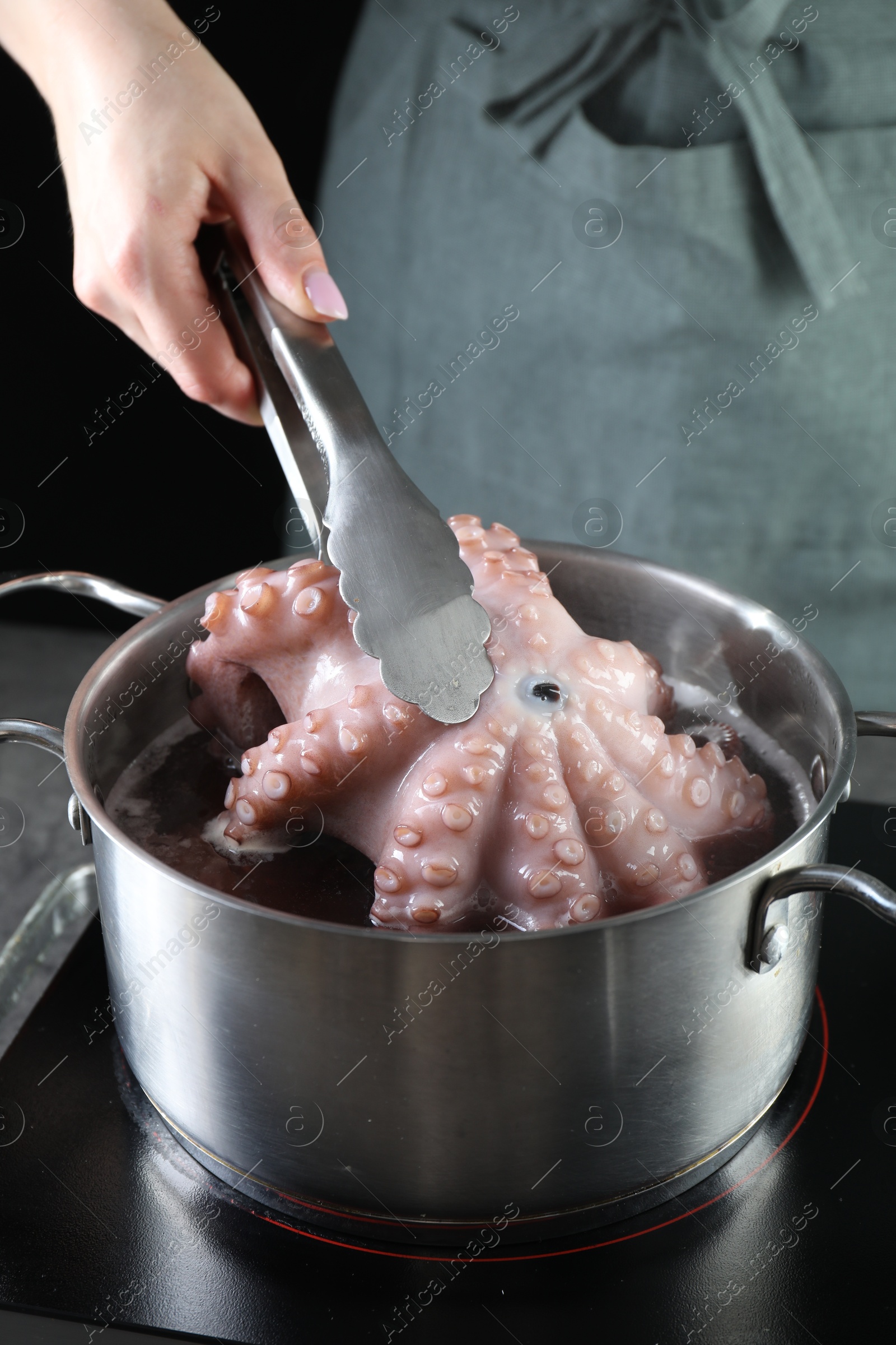 Photo of Woman taking boiled octopus from pan on stove, closeup