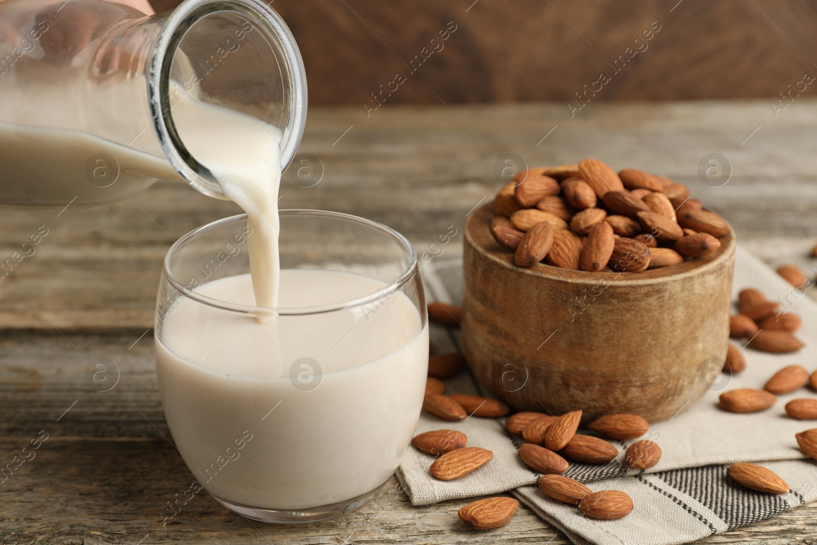 Photo of Pouring almond milk into glass and nuts at wooden table, closeup