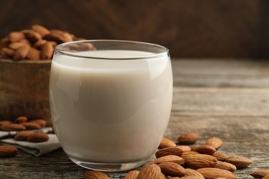 Photo of Fresh almond milk in glass and nuts on wooden table, closeup