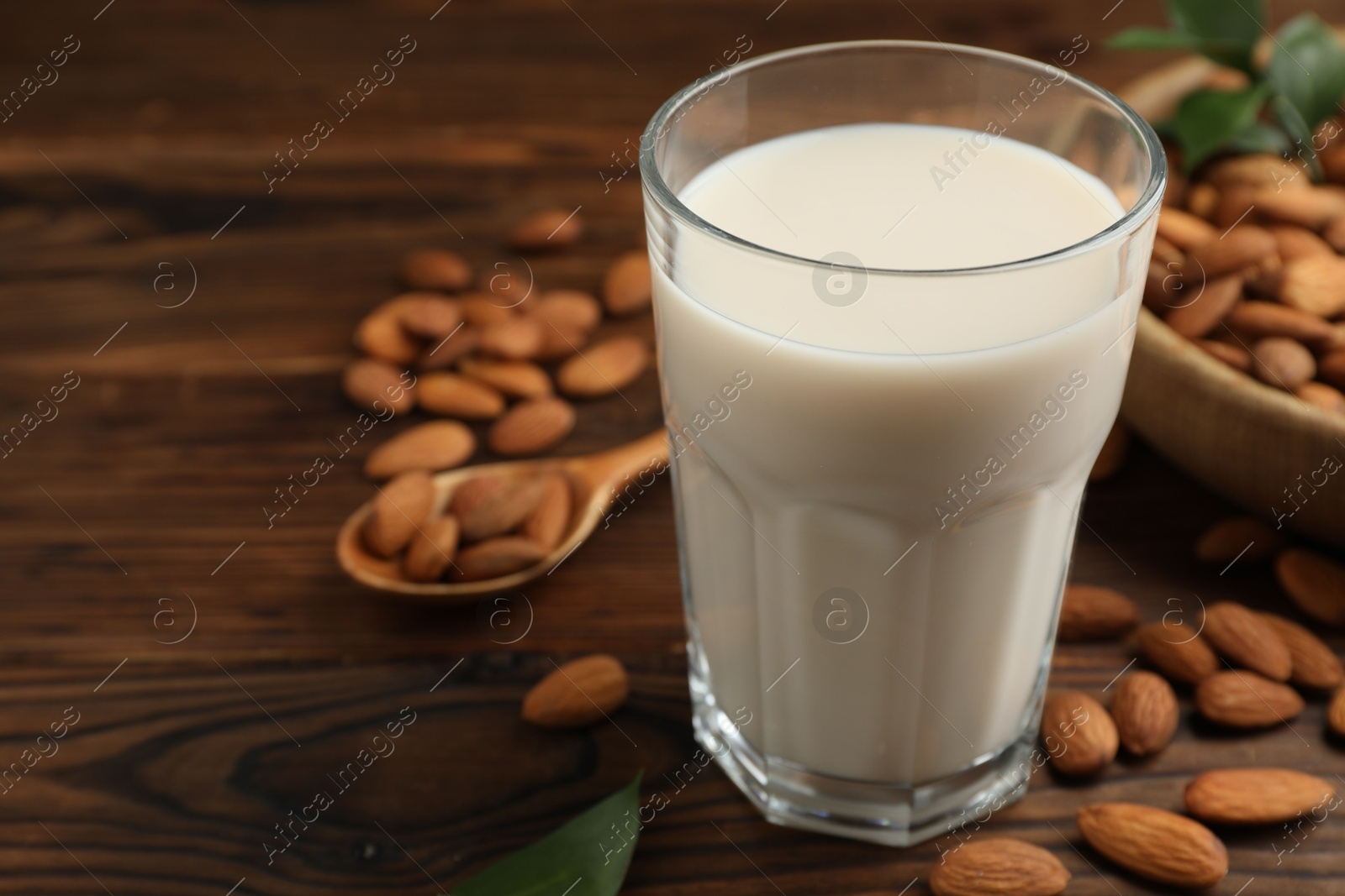 Photo of Fresh almond milk in glass and nuts on wooden table, closeup