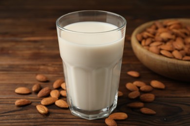 Fresh almond milk in glass and nuts on wooden table, closeup