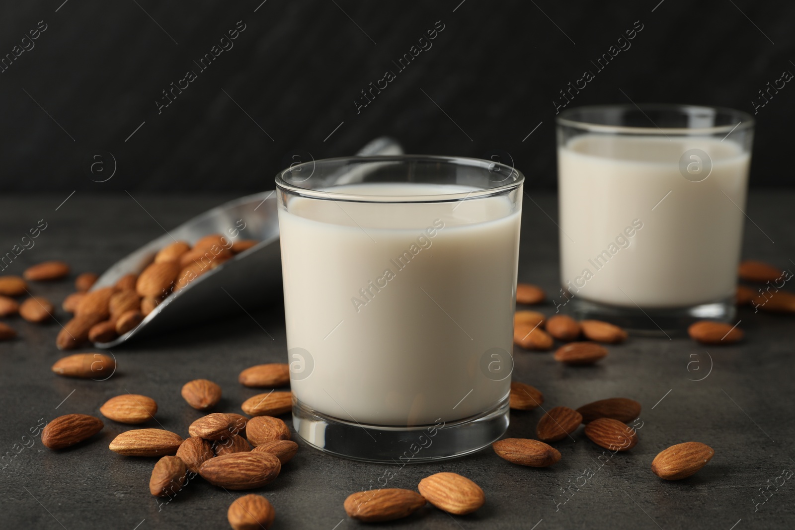 Photo of Fresh almond milk in glasses and nuts on dark grey table, closeup