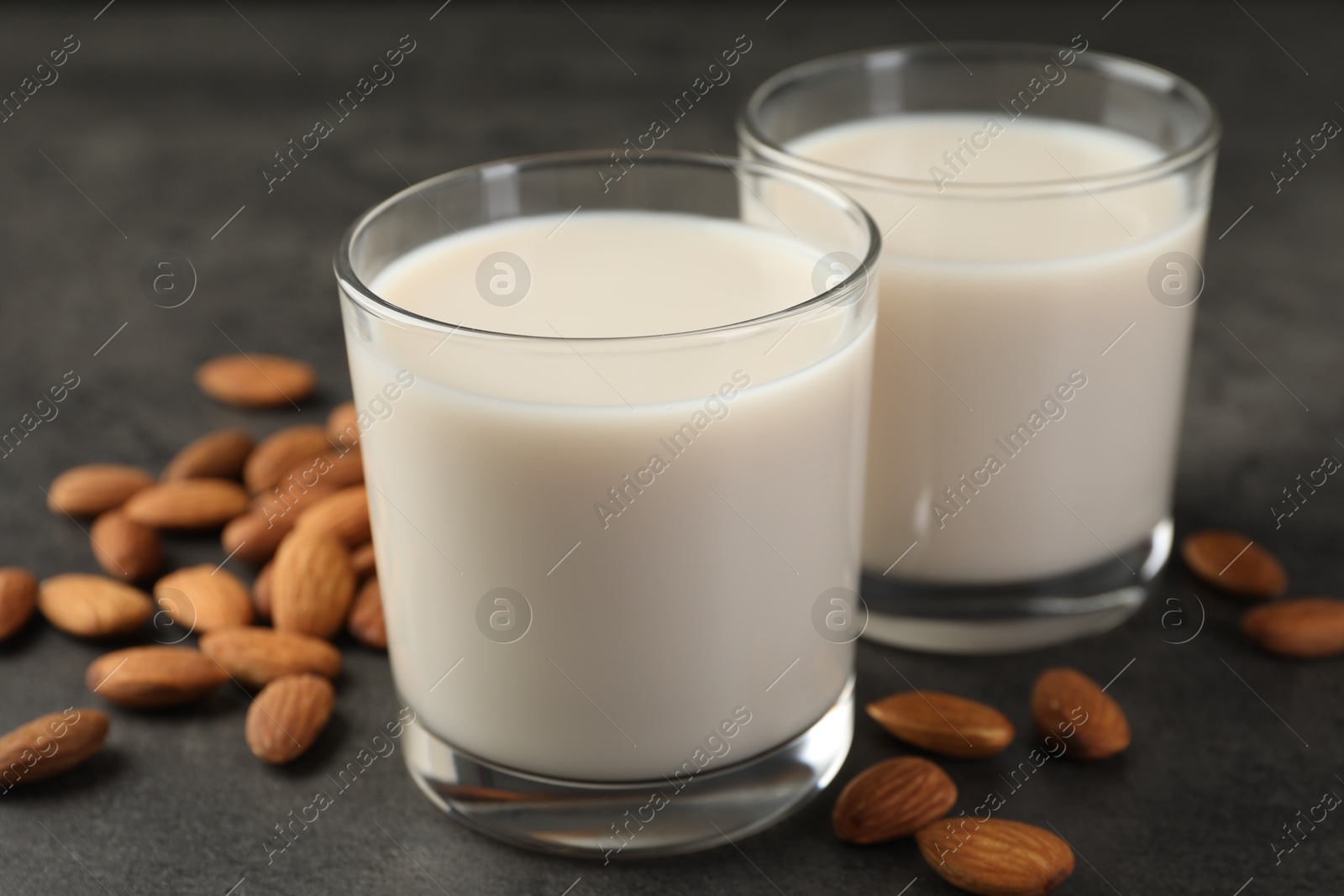 Photo of Fresh almond milk in glasses and nuts on dark grey table, closeup