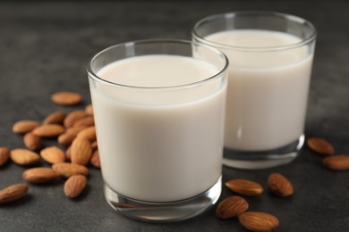 Fresh almond milk in glasses and nuts on dark grey table, closeup