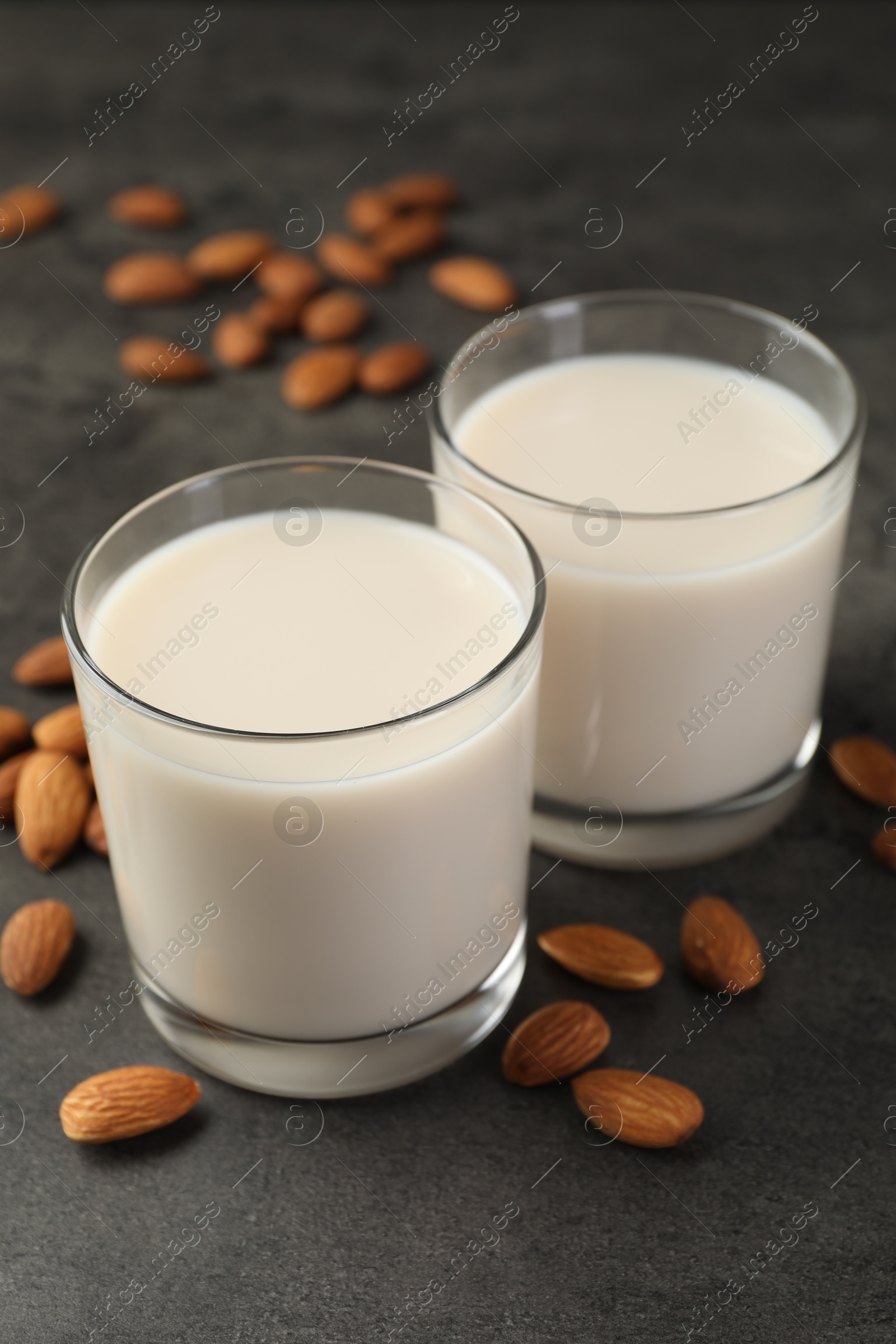 Photo of Fresh almond milk in glasses and nuts on dark grey table, closeup