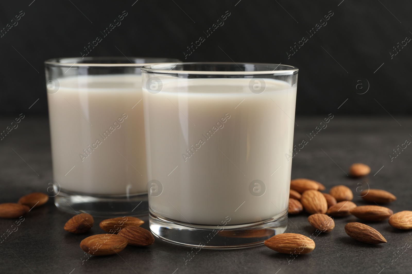 Photo of Fresh almond milk in glasses and nuts on dark grey table, closeup