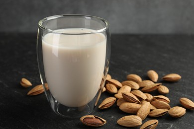 Photo of Fresh almond milk in glass and nuts on black table, closeup