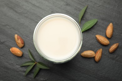 Photo of Fresh almond milk in glass, nuts and leaves on black table, top view