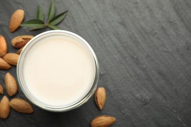 Fresh almond milk in glass, nuts and leaves on black table, top view. Space for text