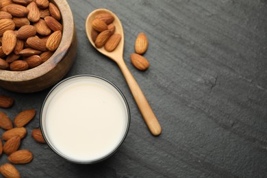 Fresh almond milk in glass, spoon and nuts on black table, top view. Space for text