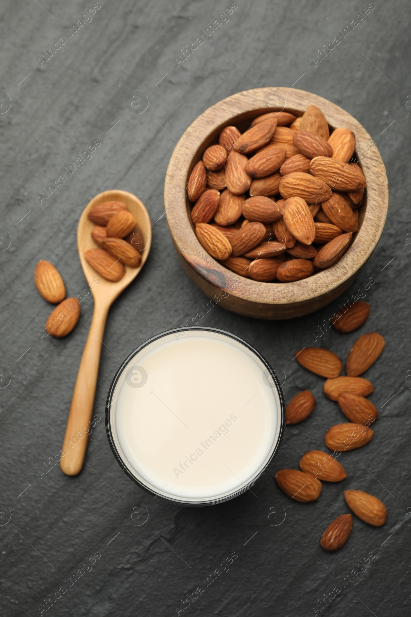 Photo of Fresh almond milk in glass, spoon and nuts on black table, top view