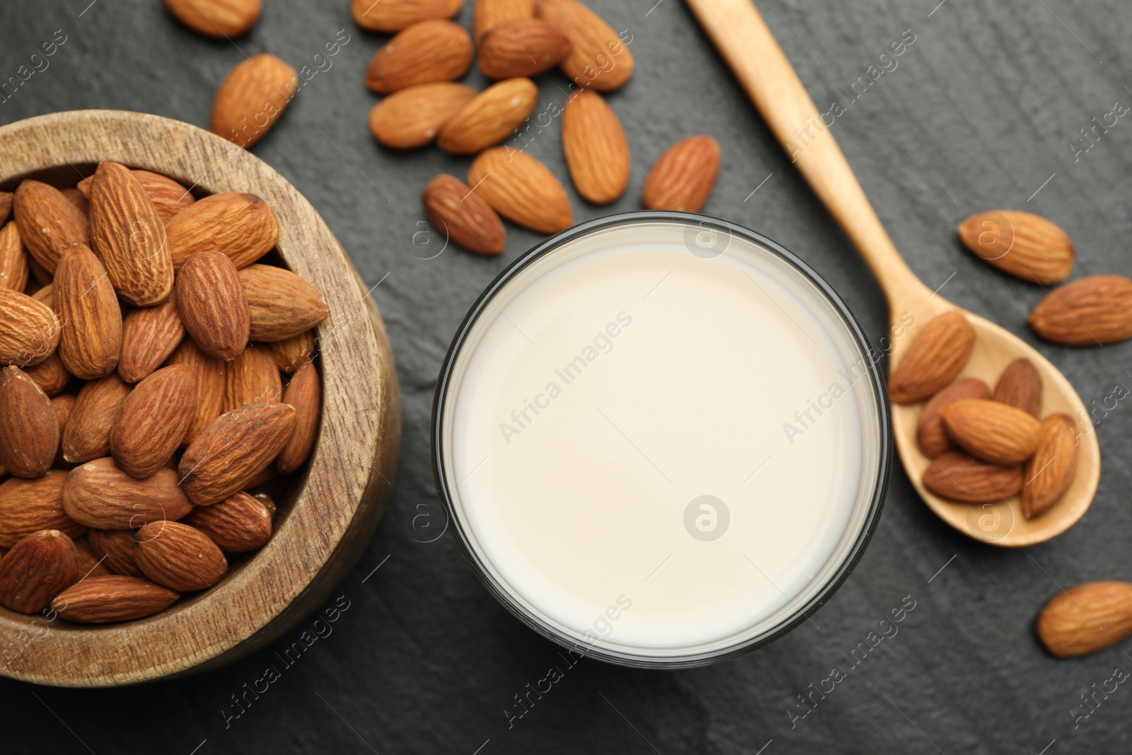 Photo of Fresh almond milk in glass, spoon and nuts on black table, top view