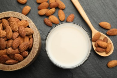 Photo of Fresh almond milk in glass, spoon and nuts on black table, top view