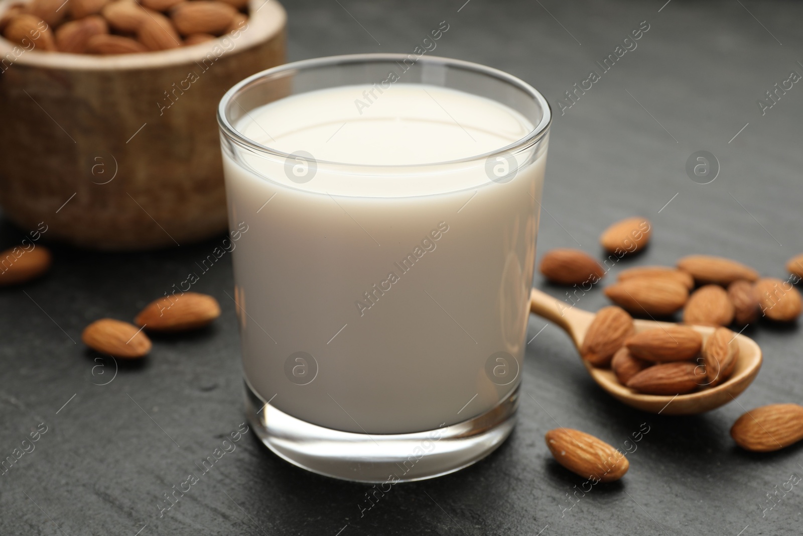 Photo of Fresh almond milk in glass, spoon and nuts on black table, closeup