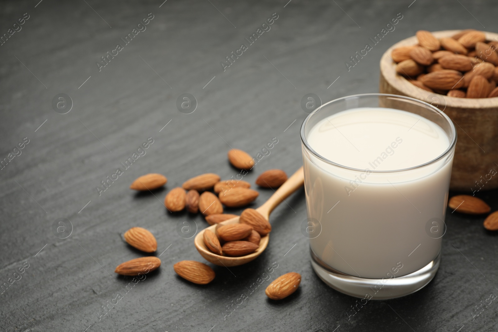 Photo of Fresh almond milk in glass, spoon and nuts on black table, closeup