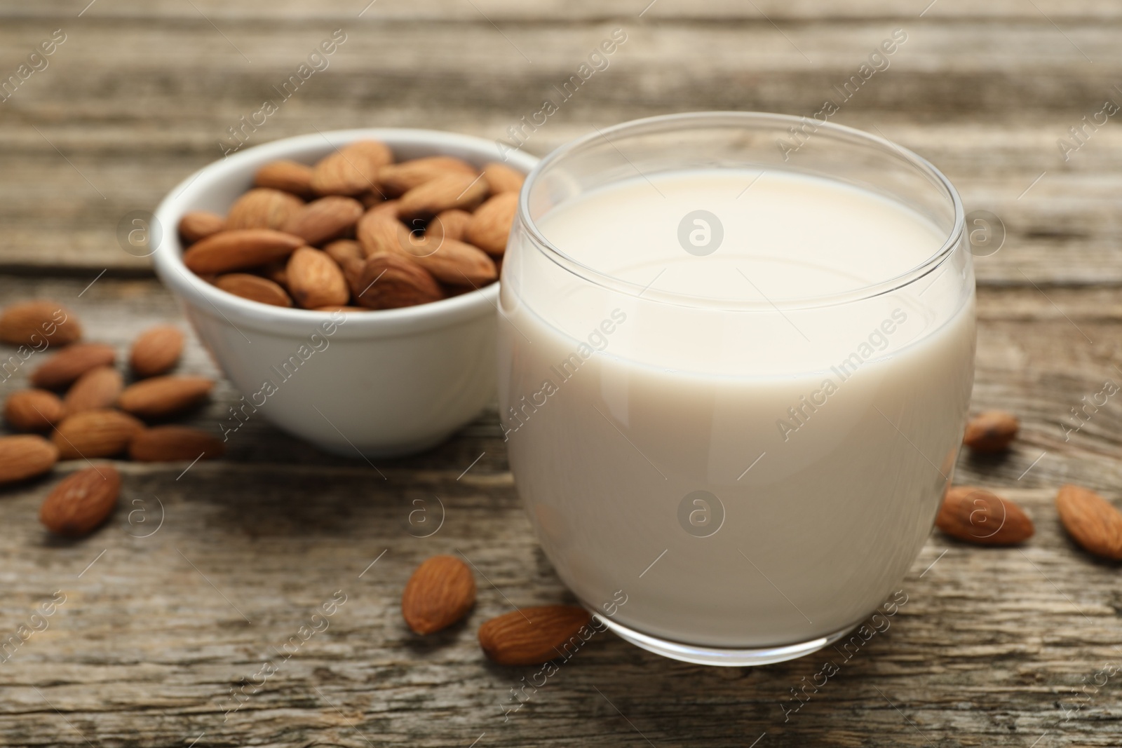 Photo of Fresh almond milk in glass and nuts on wooden table, closeup