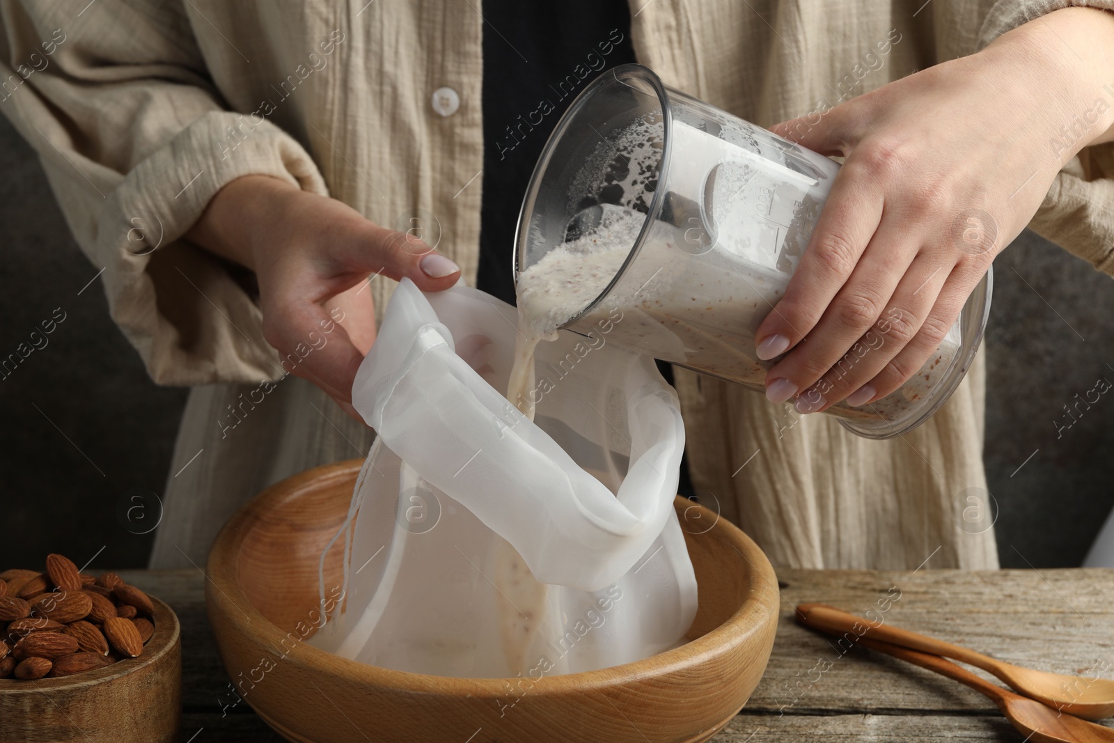 Photo of Making almond milk. Woman pouring nut mixture into cheesecloth at wooden table, closeup