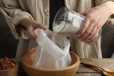 Photo of Making almond milk. Woman pouring nut mixture into cheesecloth at wooden table, closeup