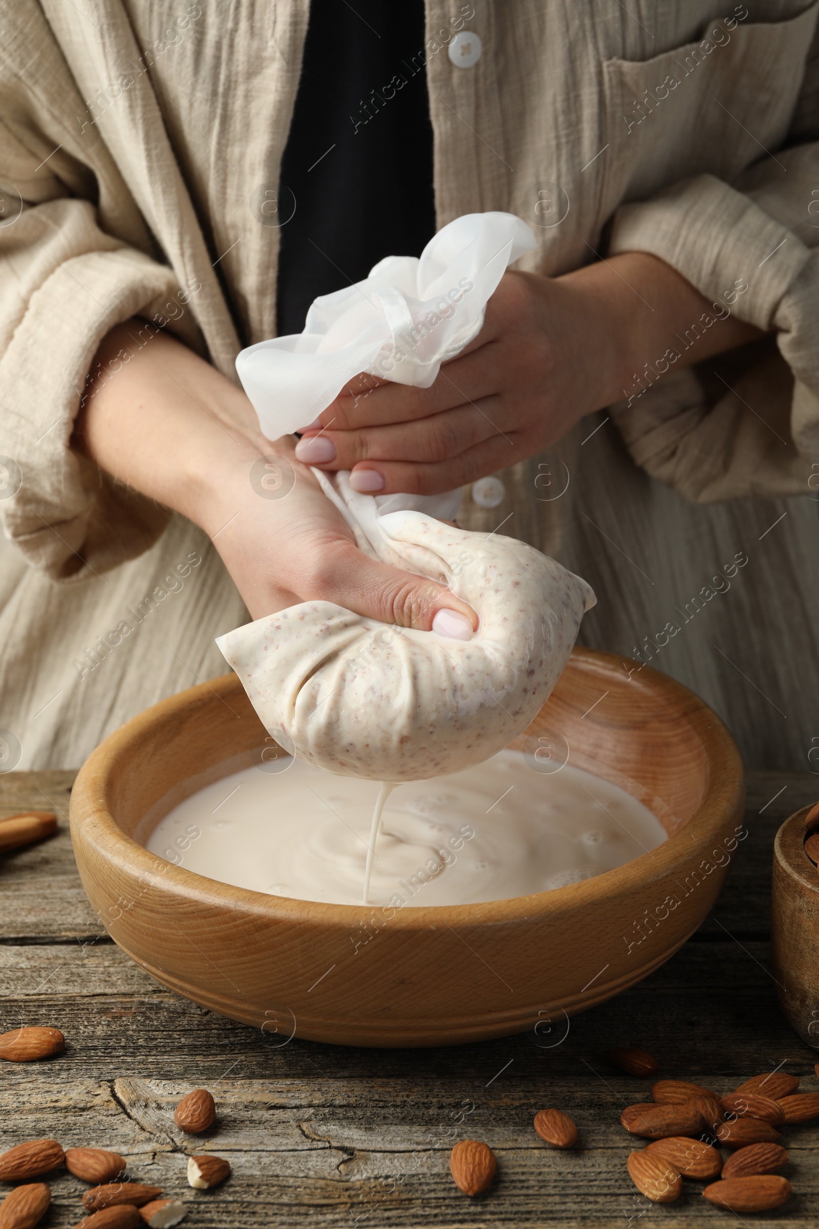 Photo of Woman making almond milk at wooden table, closeup