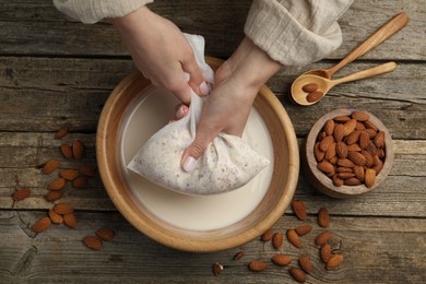 Woman making almond milk at wooden table, top view