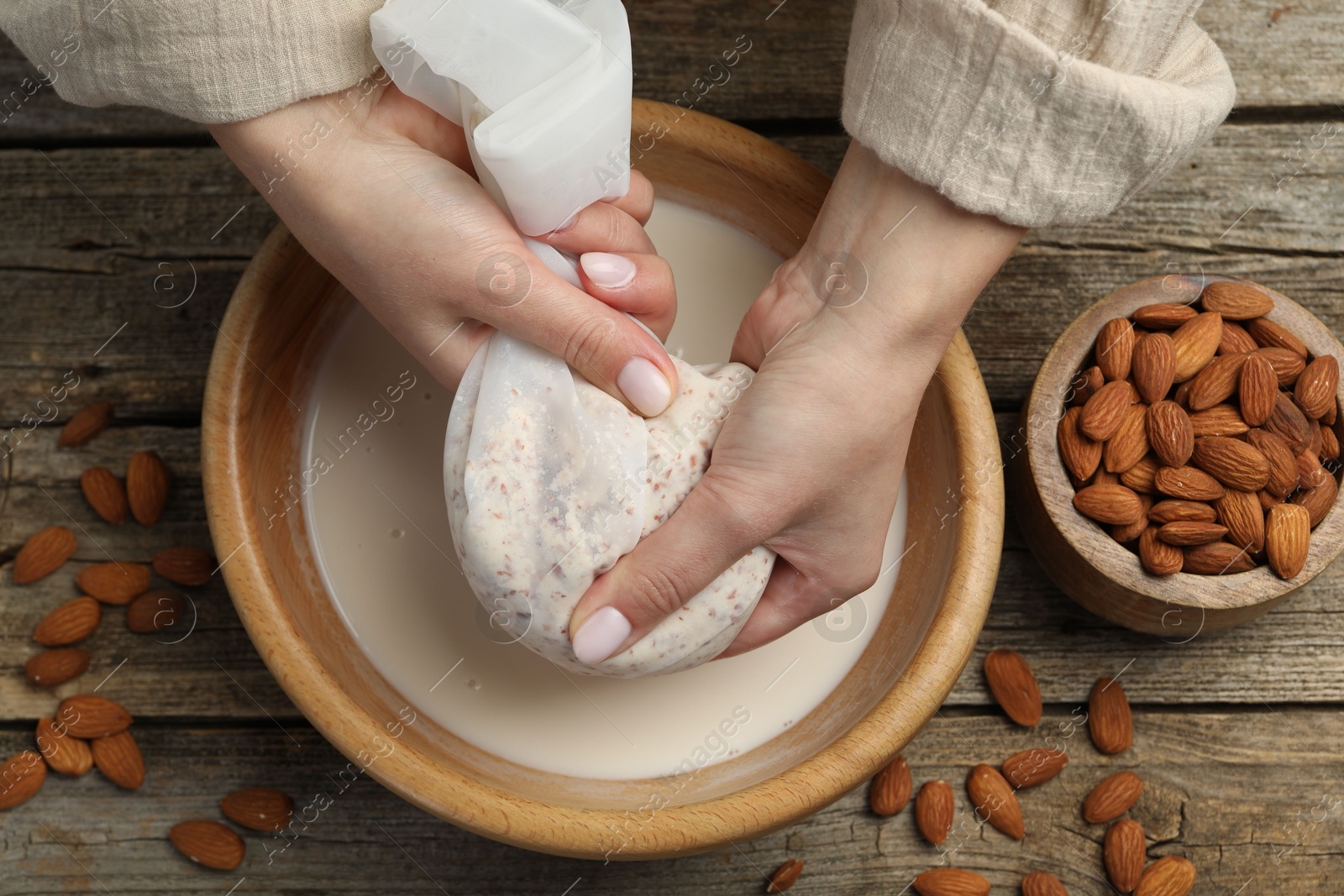 Photo of Woman making almond milk at wooden table, top view