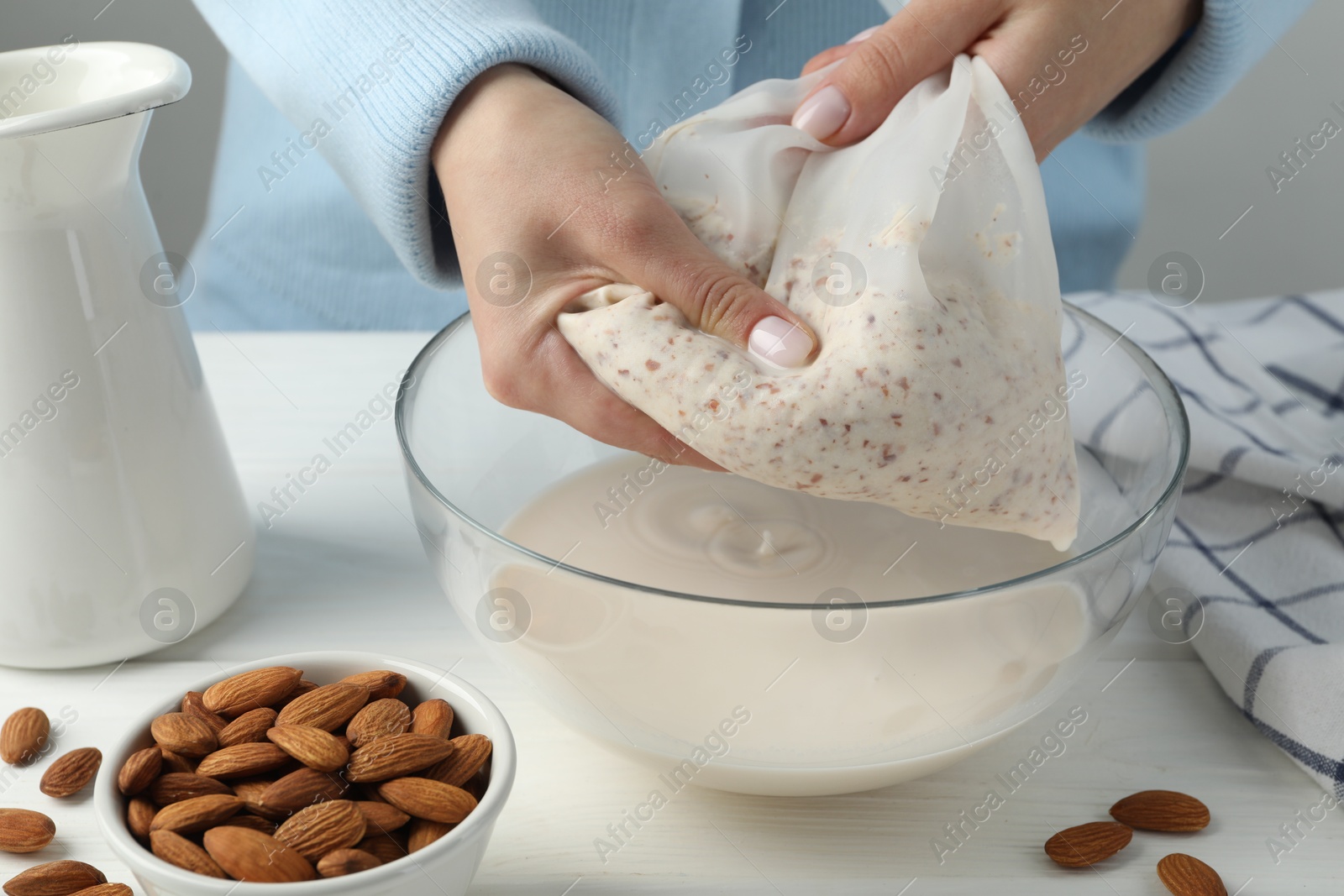 Photo of Woman making almond milk at white wooden table, closeup