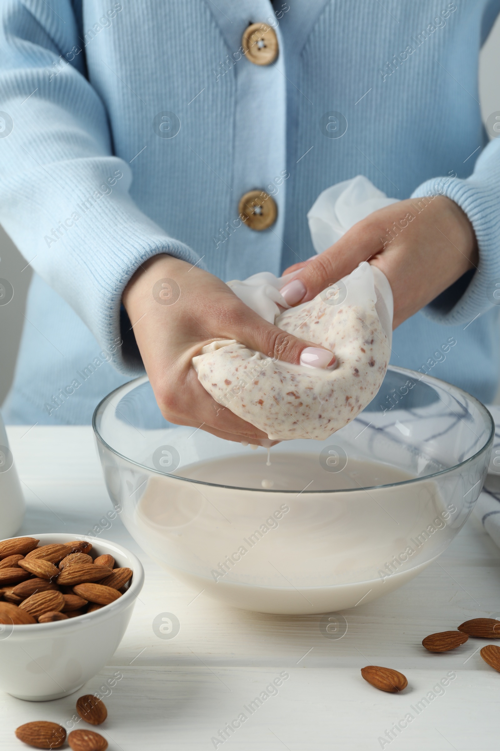 Photo of Woman making almond milk at white wooden table, closeup