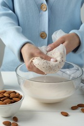 Photo of Woman making almond milk at white wooden table, closeup