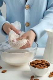 Photo of Woman making almond milk at white wooden table, closeup