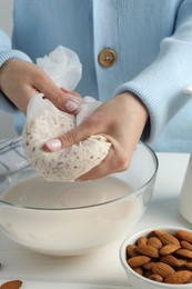 Photo of Woman making almond milk at white wooden table, closeup